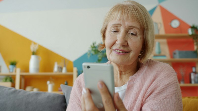 A smiling older woman using her phone at home